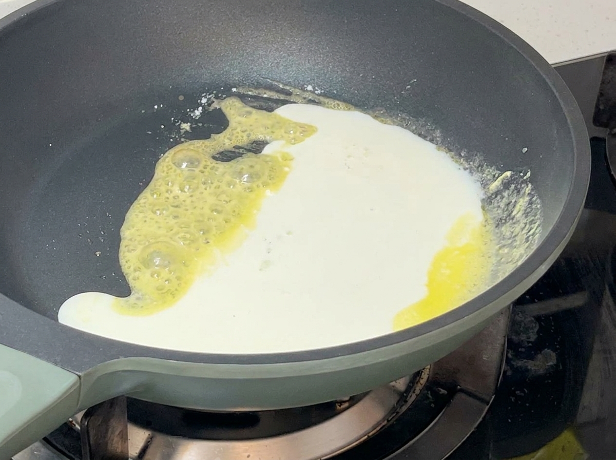 Mezcla blanca de lácteos vertiéndose en la sartén con el roux amarillo creando una salsa espesa.