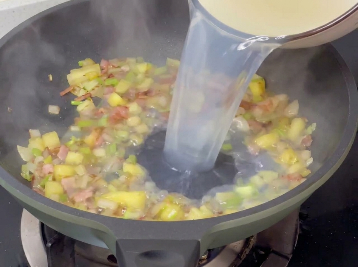 Vertiendo el caldo claro de almejas en la sartén con las verduras y el bacon.