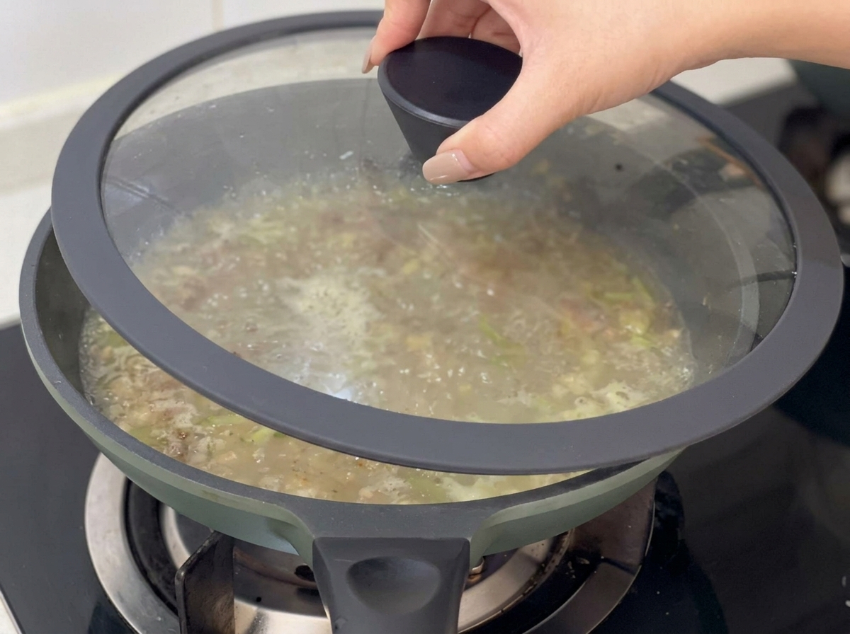 Mano colocando una tapa de cristal sobre la sartén con la base del clam chowder.