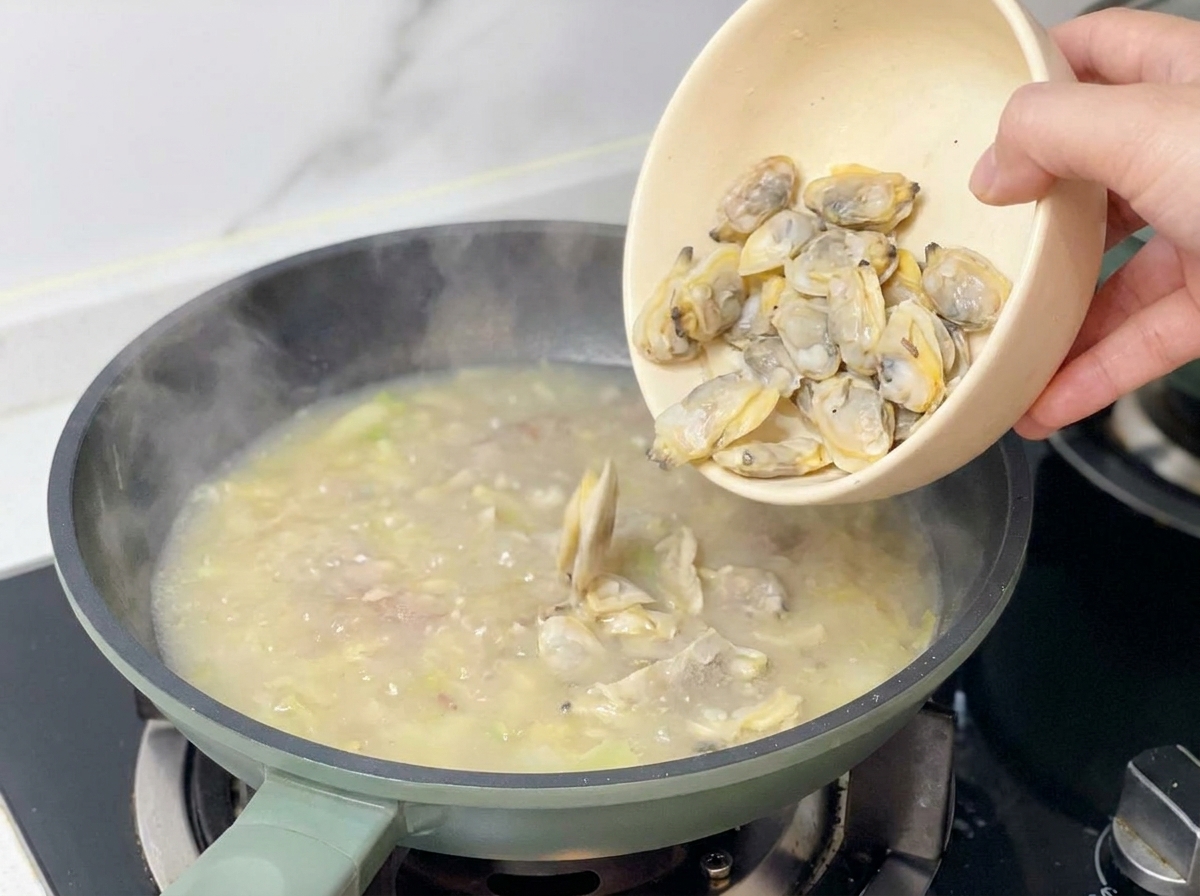 Mano añadiendo la carne de las almejas desde un cuenco beige a la sopa hirviendo.