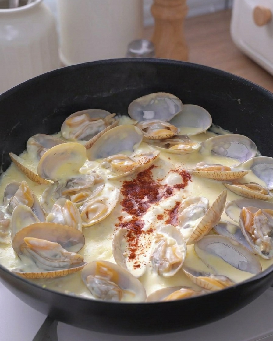 Una pizca de especia roja espolvoreada en el centro de la sartén con almejas cremosas.