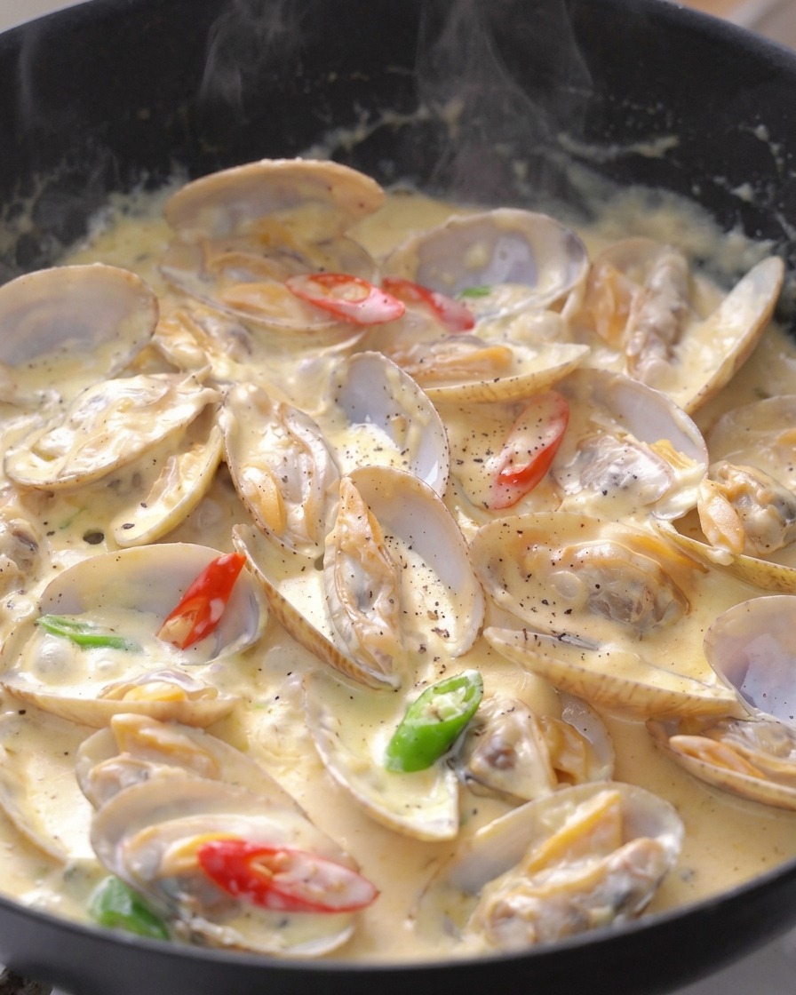 Almejas cremosas en una sartén, decoradas con rodajas de chile rojo y verde y pimienta negra molida.