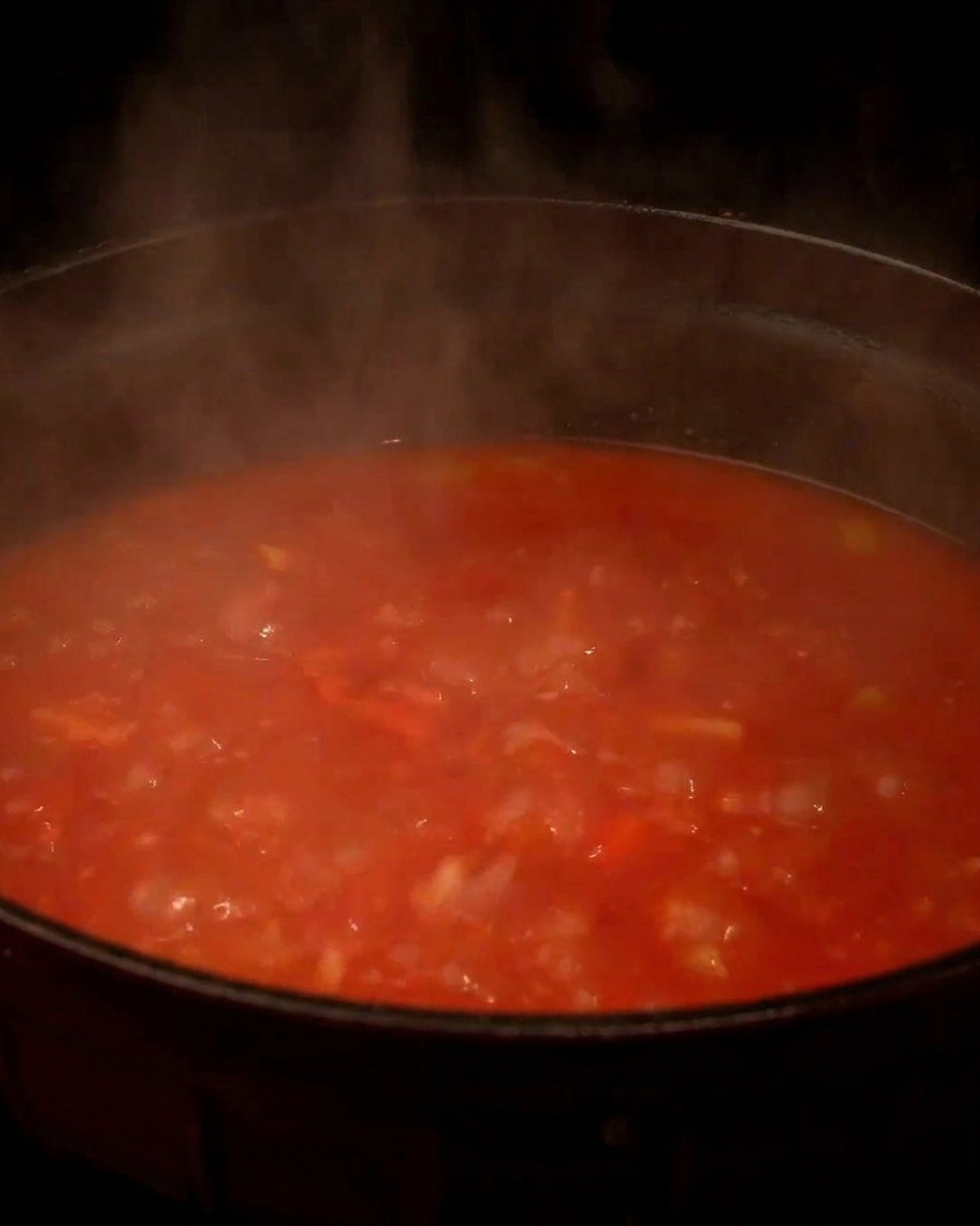 Una olla humeante y burbujeante de clam chowder con base de tomate rojo hirviendo a fuego lento en la estufa.
