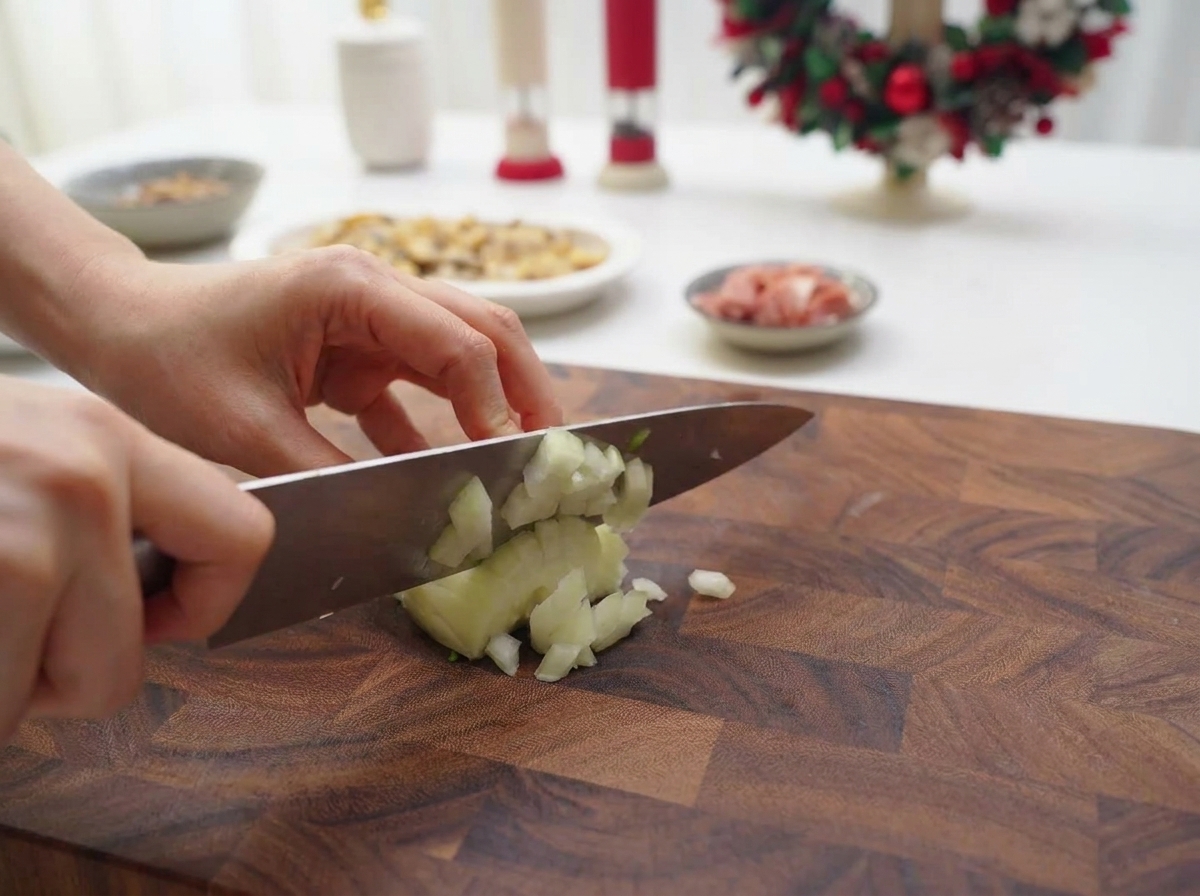 Manos usando un cuchillo de chef para picar una cebolla blanca en trozos finos sobre una tabla de madera.