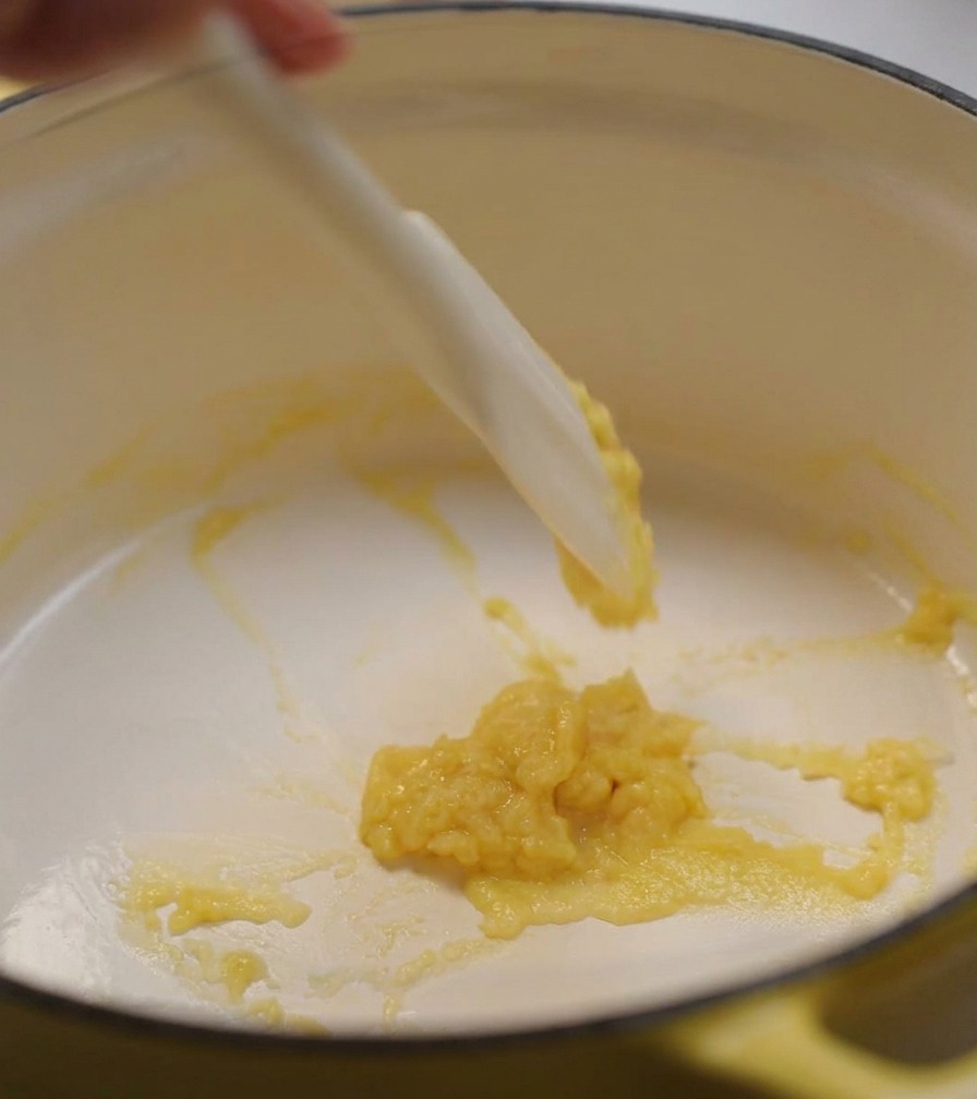 Una espátula de silicona blanca removiendo una pasta espesa de mantequilla y harina en una olla amarilla.