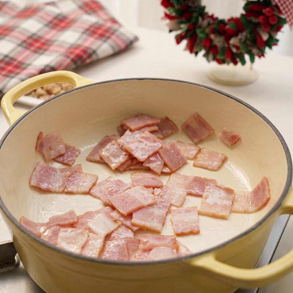 Trozos de bacon picado friéndose y soltando su grasa en una olla de esmalte amarillo claro.