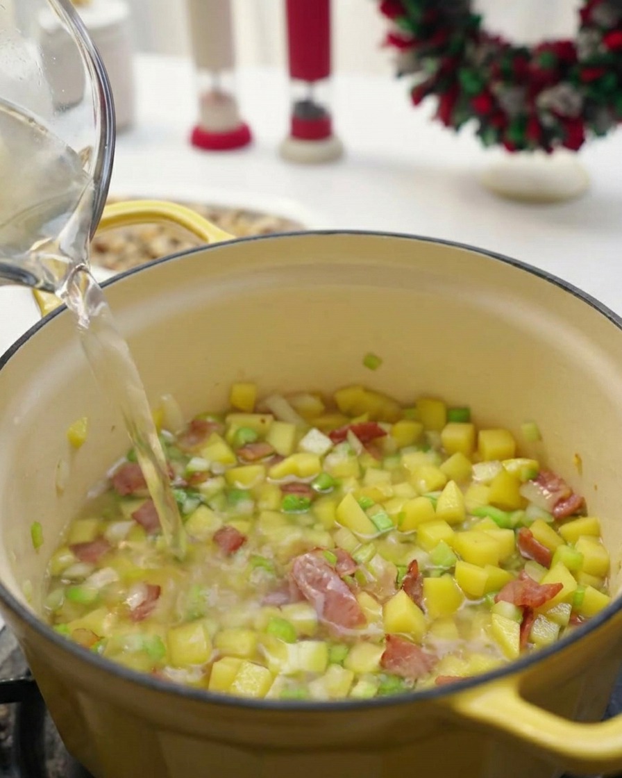 Líquido transparente vertiéndose desde una jarra de cristal a una olla amarilla con verduras y bacon.