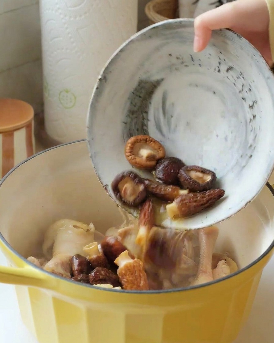 Un bol con shiitakes y colmenillas hidratadas vertiéndose en la olla con el pollo.