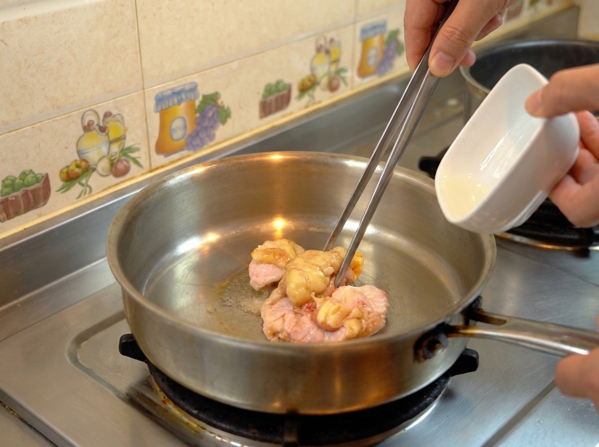 Trozos de grasa de pollo cruda en una sartén soltando aceite dorado.