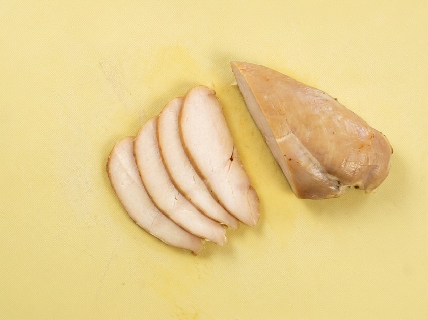 Láminas uniformes de pechuga de pollo cocida sobre una tabla de cortar.