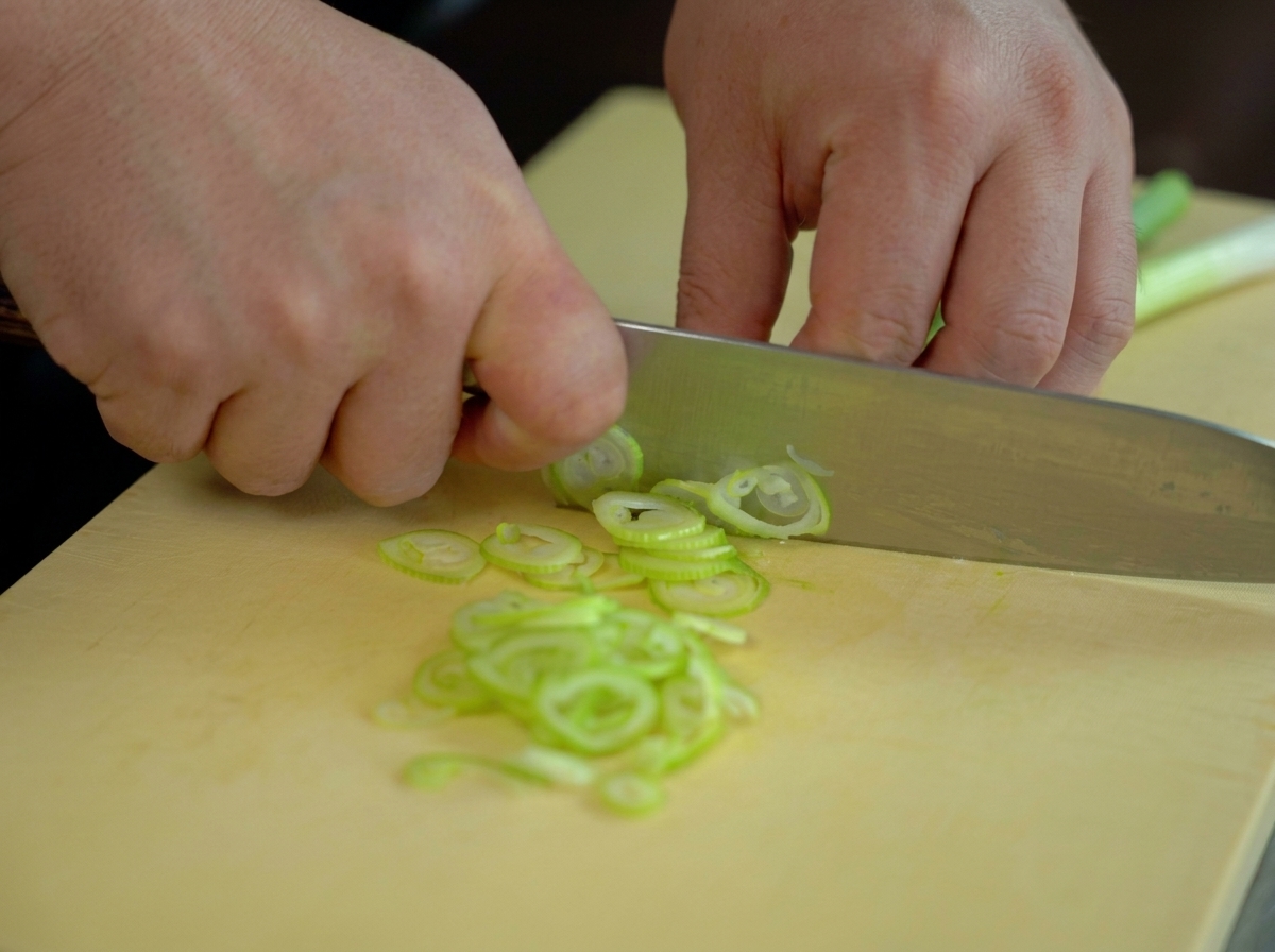 Manos picando cebolleta fresca en aros finos sobre una tabla amarilla.