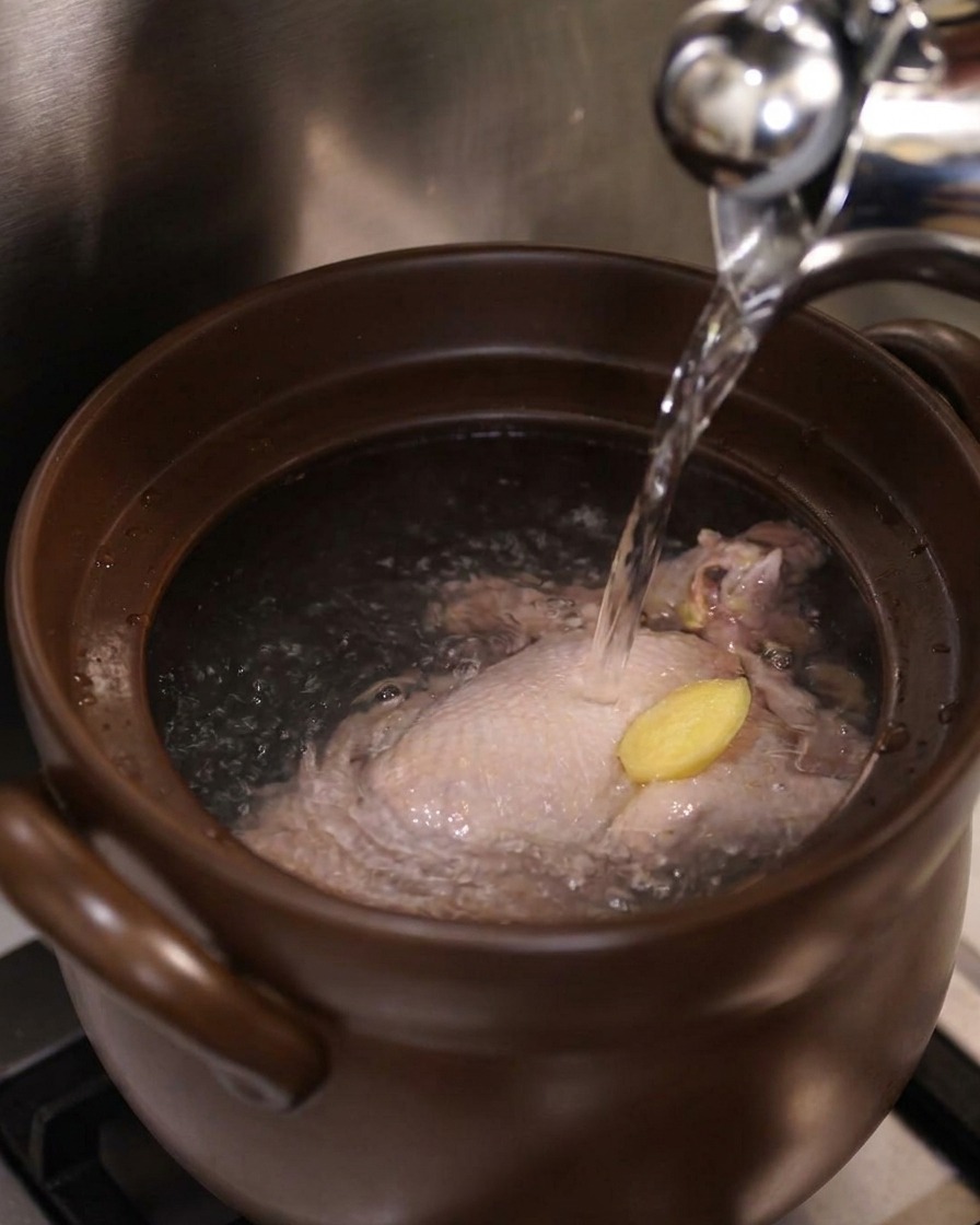 Agua hirviendo cayendo sobre el pollo y el jengibre dentro de la olla de cerámica.