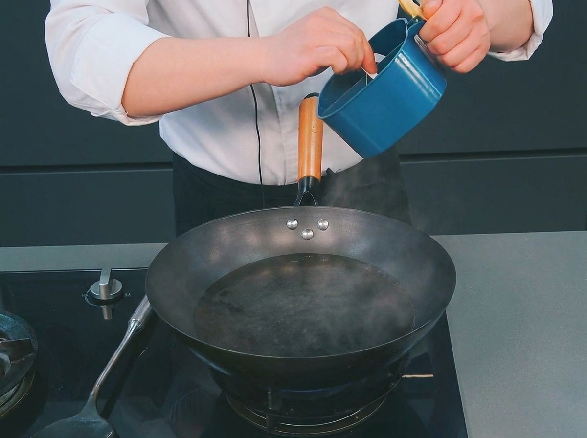 Un chef añadiendo una pequeña cucharada de sal desde un recipiente azul a un wok con agua hirviendo.
