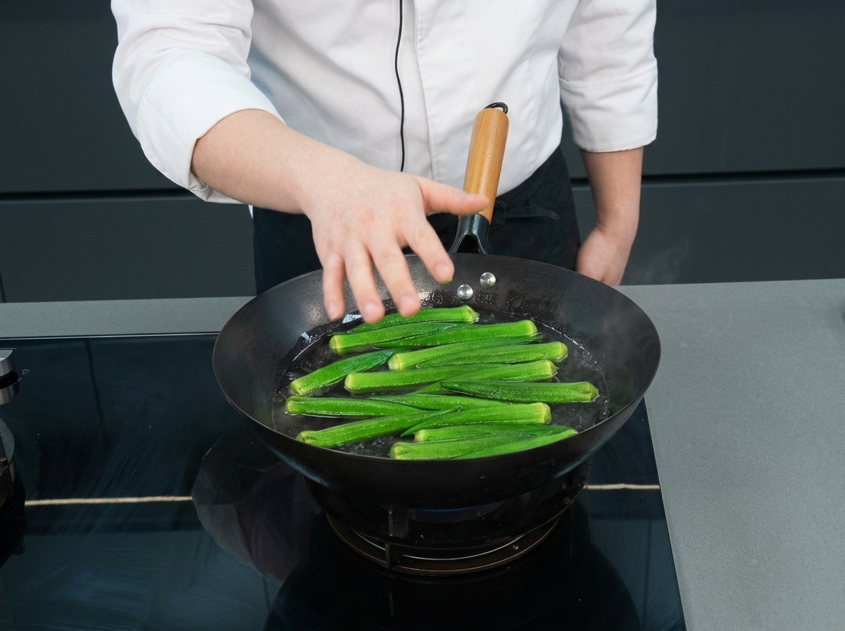 Okra verde entera flotando en un wok con agua hirviendo mientras la mano de un chef se acerca.