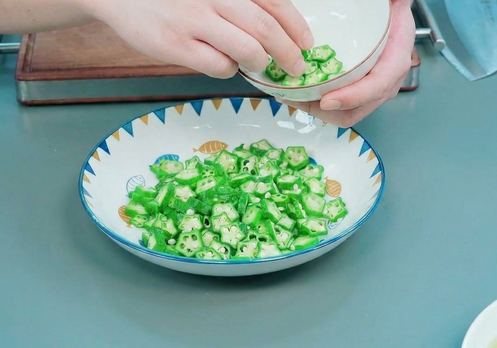 Manos colocando cuidadosamente rodajas de okra en forma de estrella en el interior de un bol blanco pequeño.