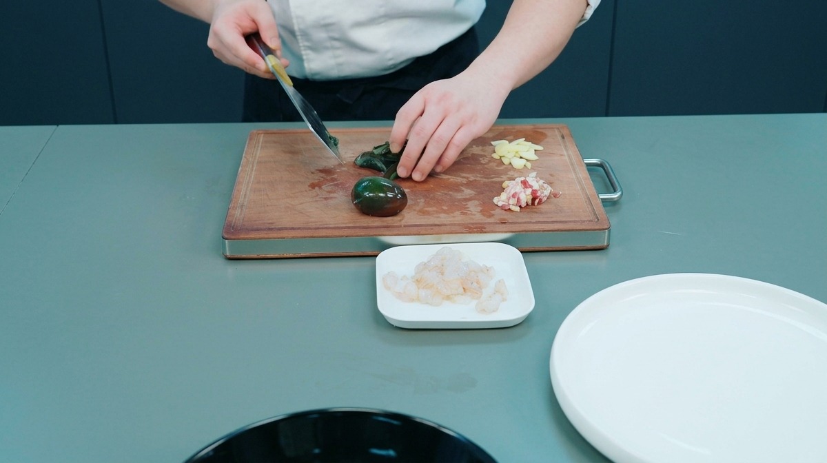 Chef cortando un huevo centenario oscuro sobre una tabla de madera junto a láminas de ajo.