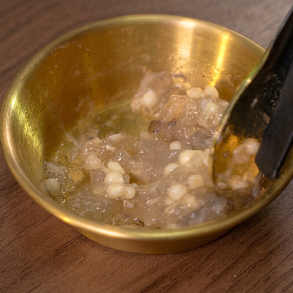 Una cuchara removiendo la pasta de gambas y semillas en un bol dorado.