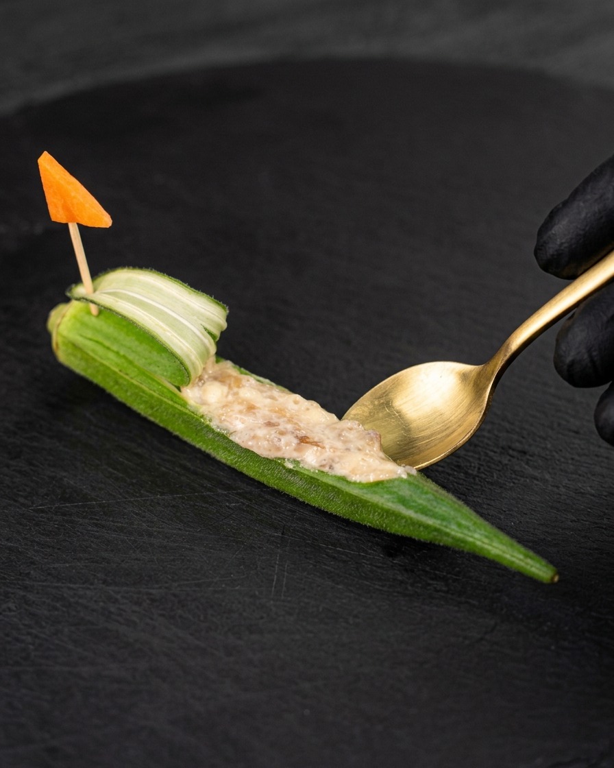 Una cuchara pequeña rellenando el quimbombó con la pasta de gambas.