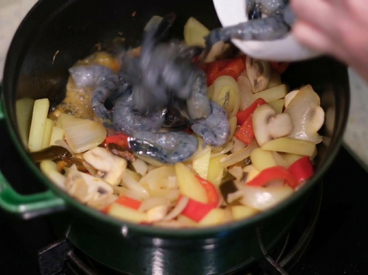 Añadiendo camarones crudos a un espacio libre en la olla con el sofrito de vegetales.