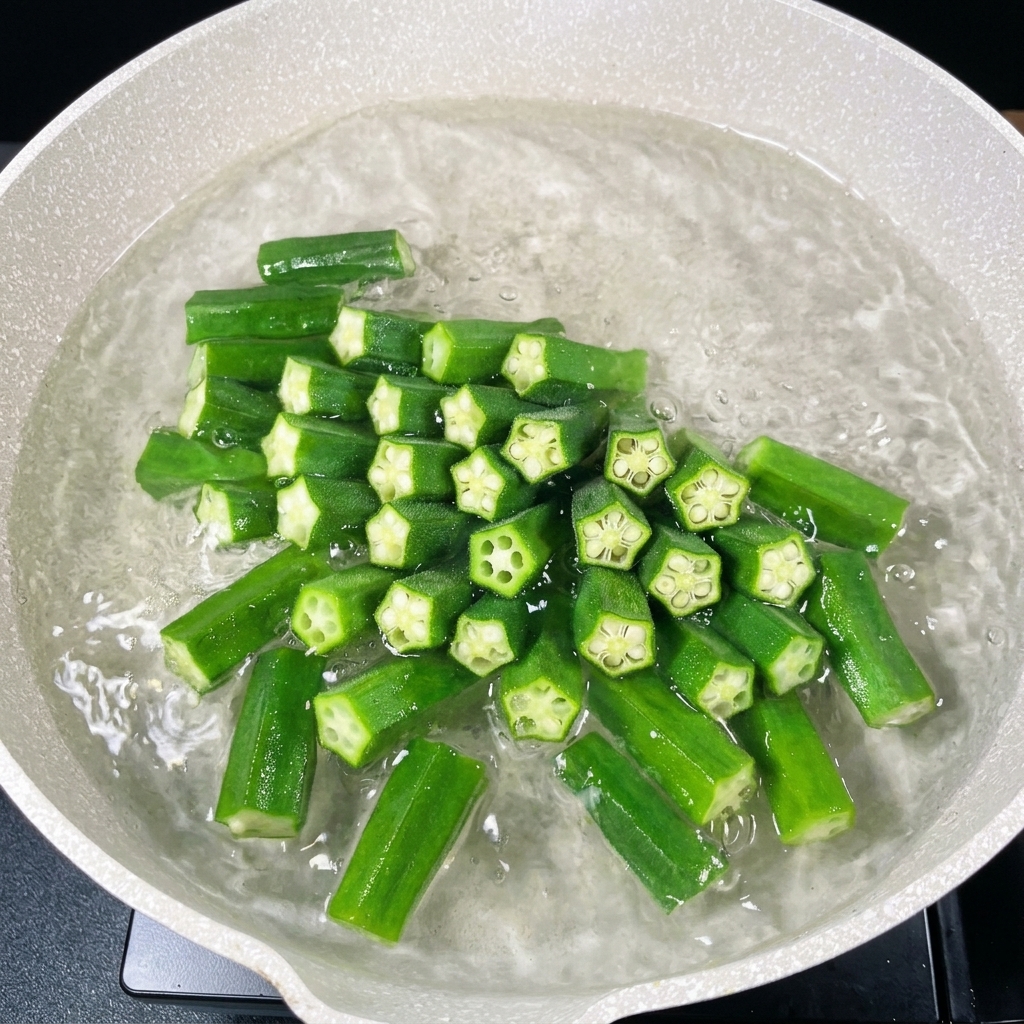 Trozos de okra verde hirviendo en una olla con agua burbujeante.