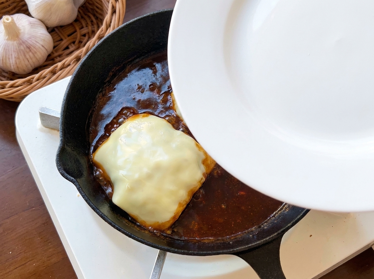 Un plato blanco usado como tapa sobre la sartén que contiene la hamburguesa con queso.