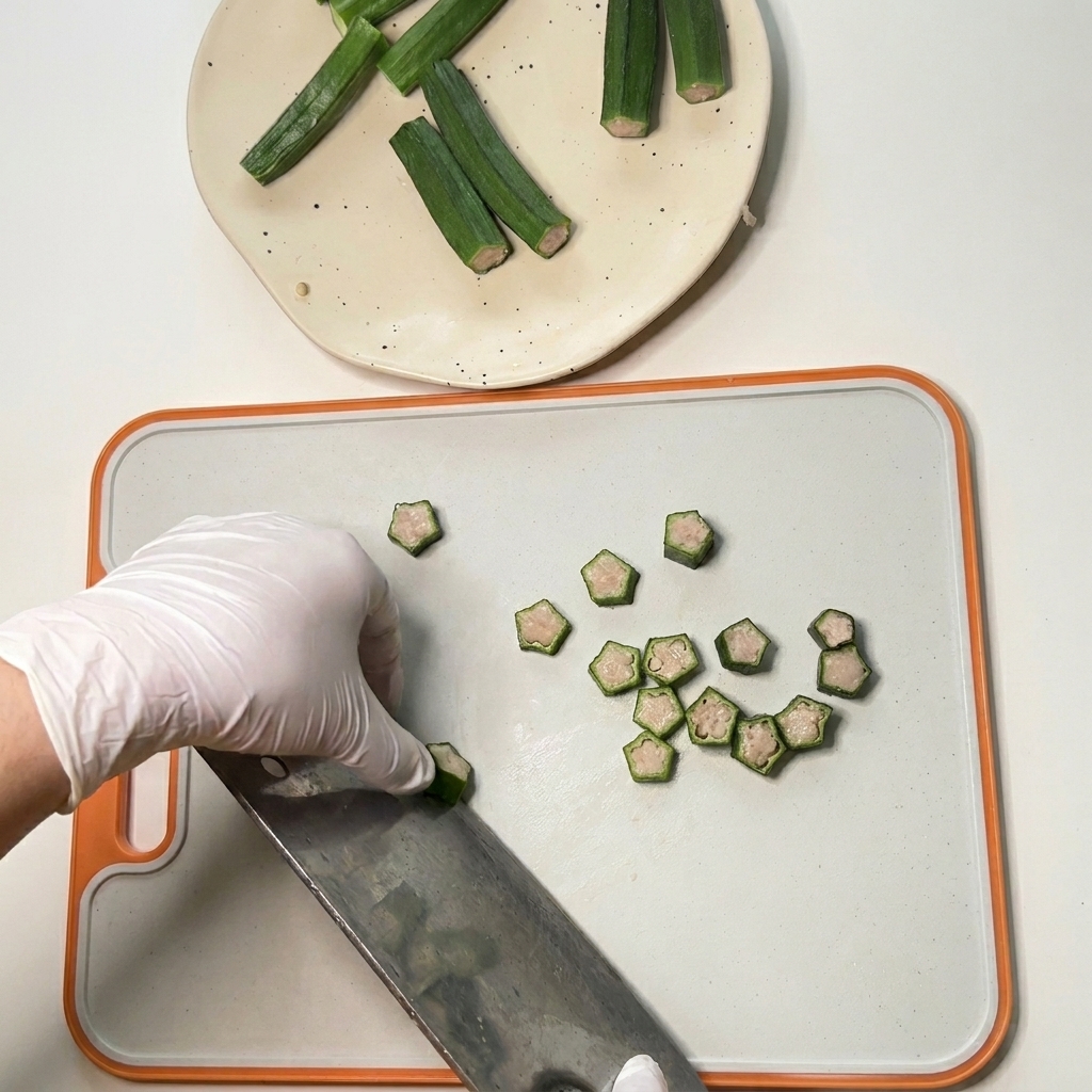 Una mano con guante usando un cuchillo de cocinero para cortar okra cruda rellena de pollo en pequeñas formas de estrella sobre una tabla de cortar.