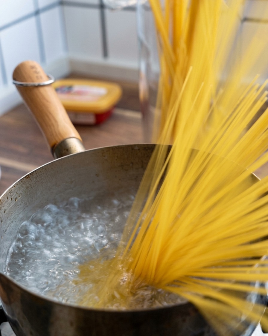 Un puñado de espaguetis secos siendo sumergidos en una olla con agua hirviendo a borbotones.