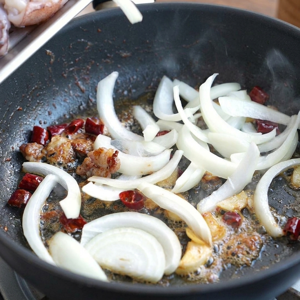 Tiras de cebolla blanca salteándose en el aceite condimentado con ajo y chiles.