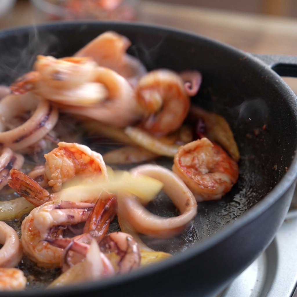 Langostinos y calamares salteándose rápidamente en una sartén caliente; los langostinos empiezan a cambiar de color.