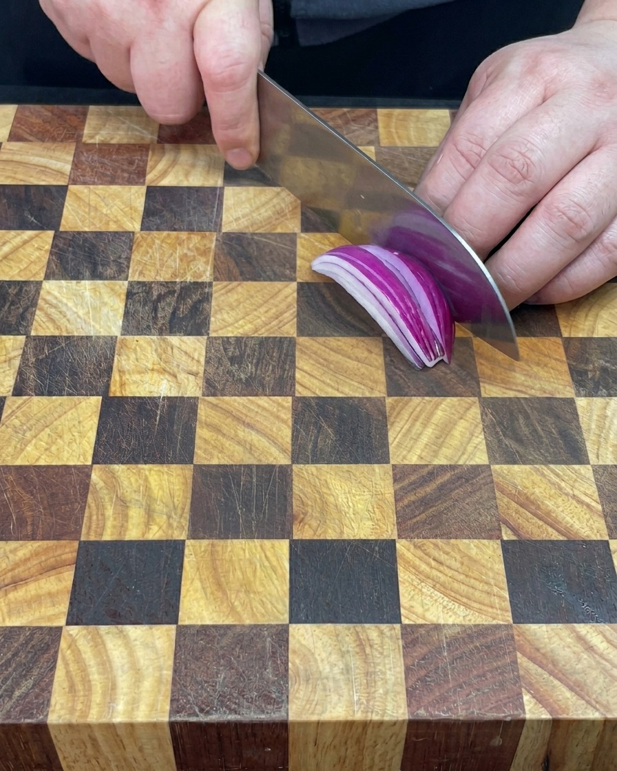 Mano picando una cebolla morada vibrante sobre una tabla de madera.