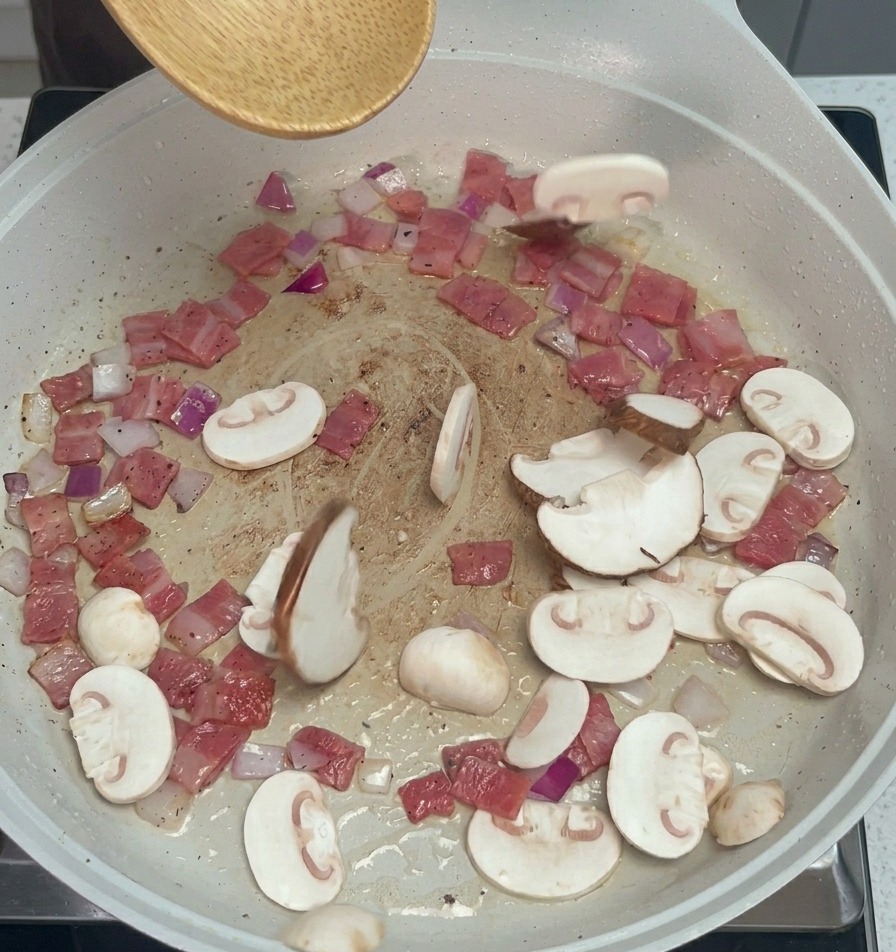 Láminas de champiñones y setas shiitake siendo incorporadas a la sartén con una cuchara de madera.