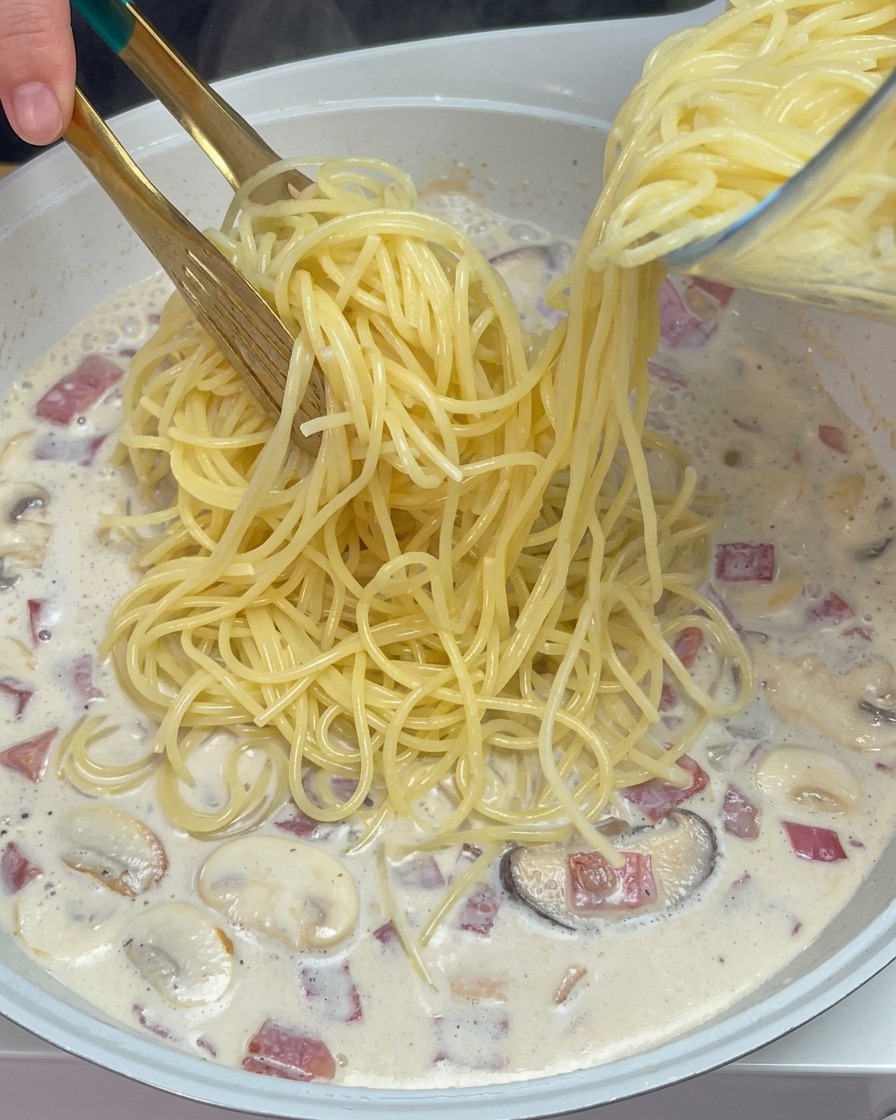 Pinzas colocando los espaguetis cocidos en la salsa cremosa de setas y bacon.