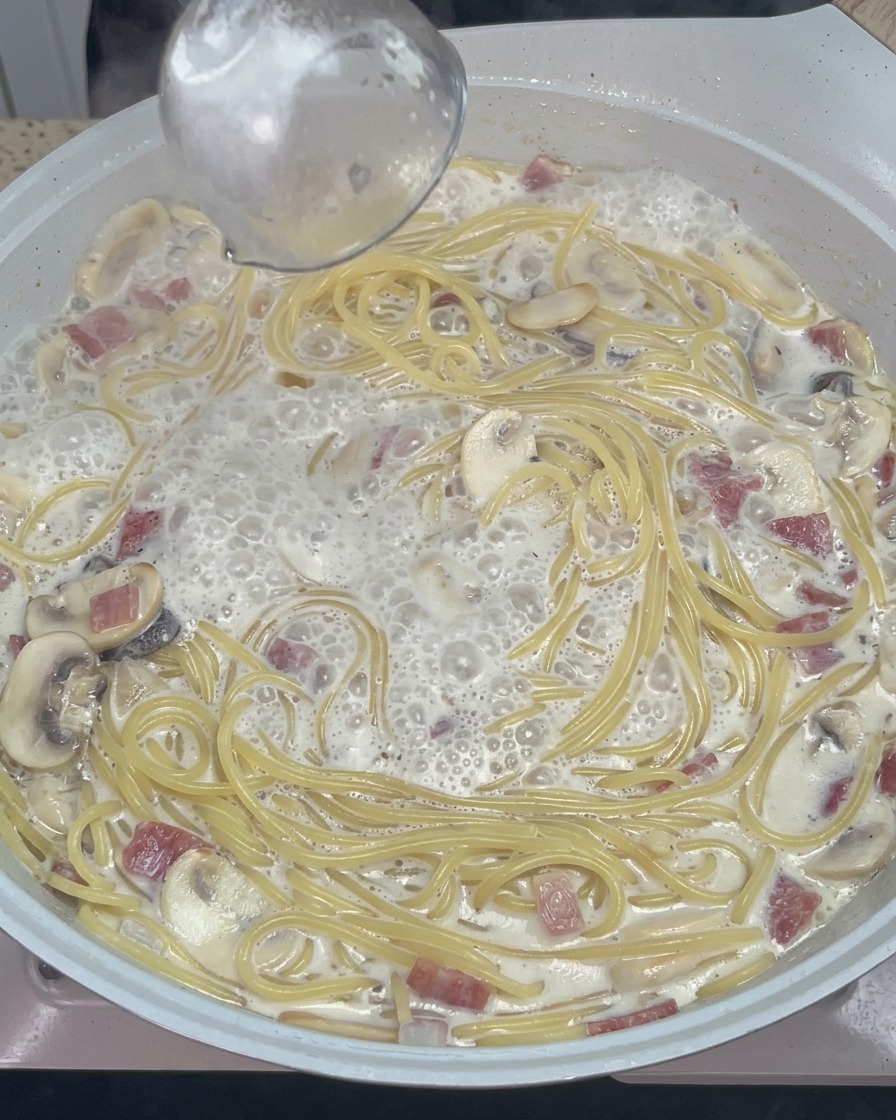Cuchara de madera removiendo pasta cremosa con queso fundido y especias en la sartén.