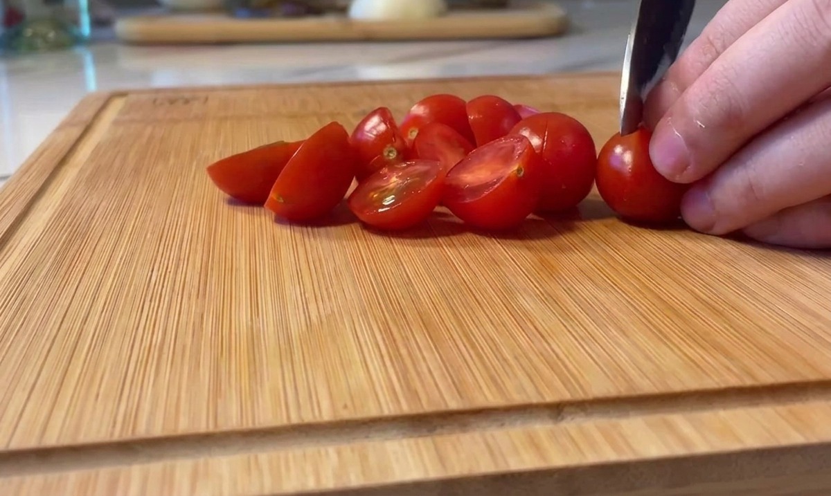 Cortando tomates cherry rojos brillantes por la mitad en una tabla de madera.