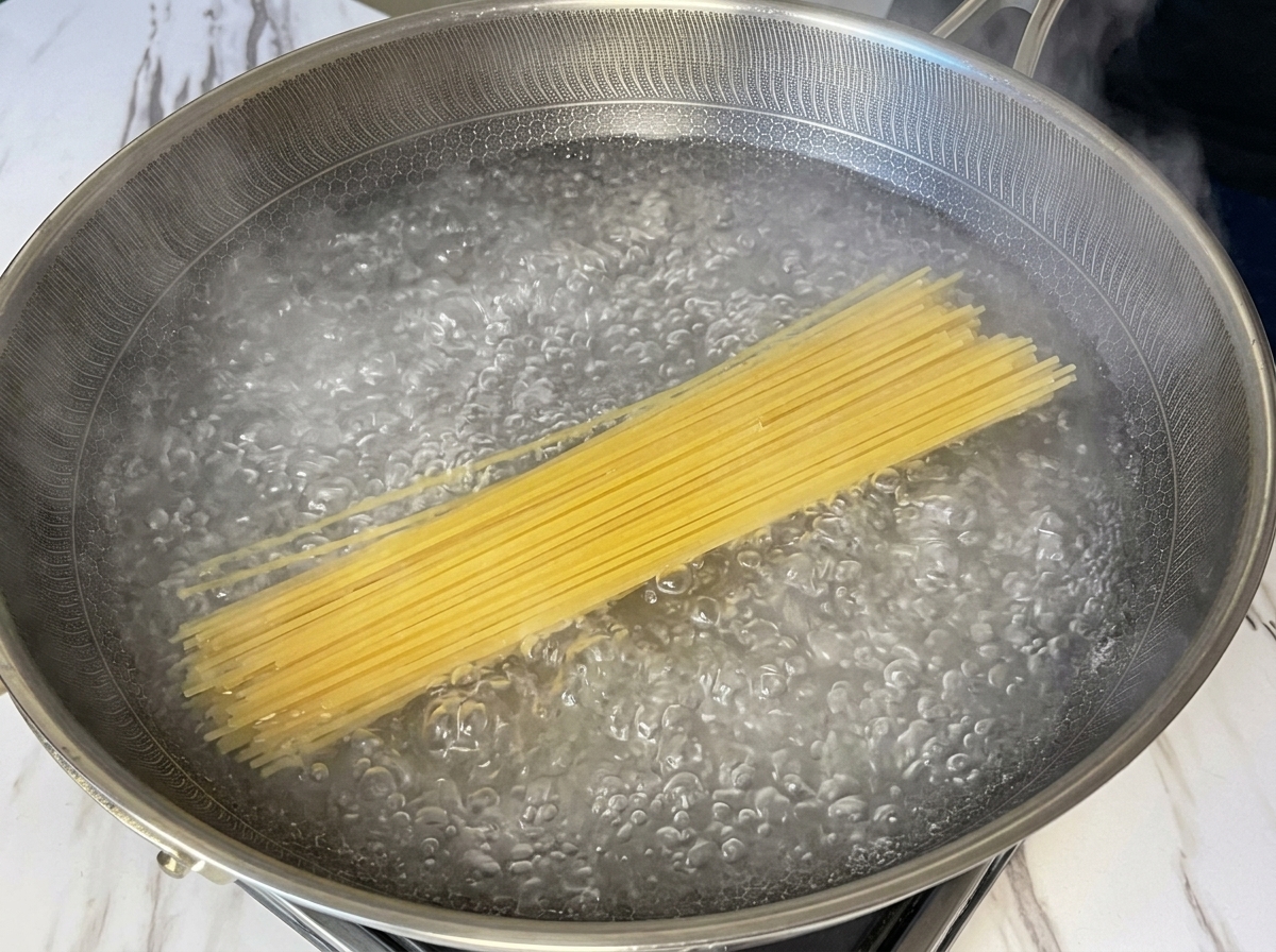 Espaguetis secos sumergidos en una sartén amplia con agua hirviendo vigorosamente.