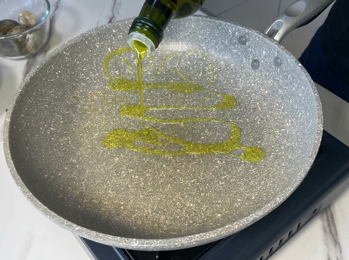 Vertiendo aceite de oliva virgen extra desde una botella verde oscura en una sartén moteada gris.