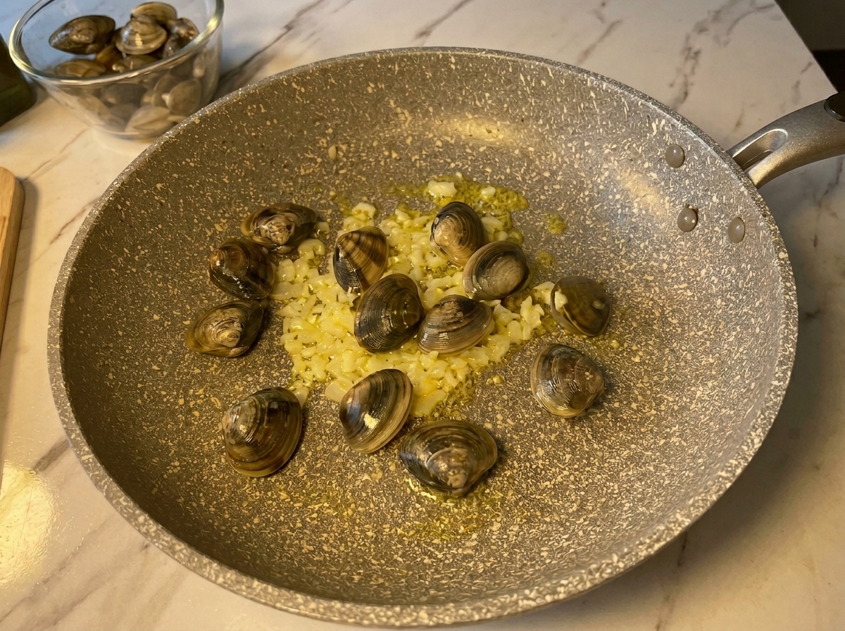 Almejas frescas y cerradas añadidas a una sartén caliente con ajo y cebollas salteadas.