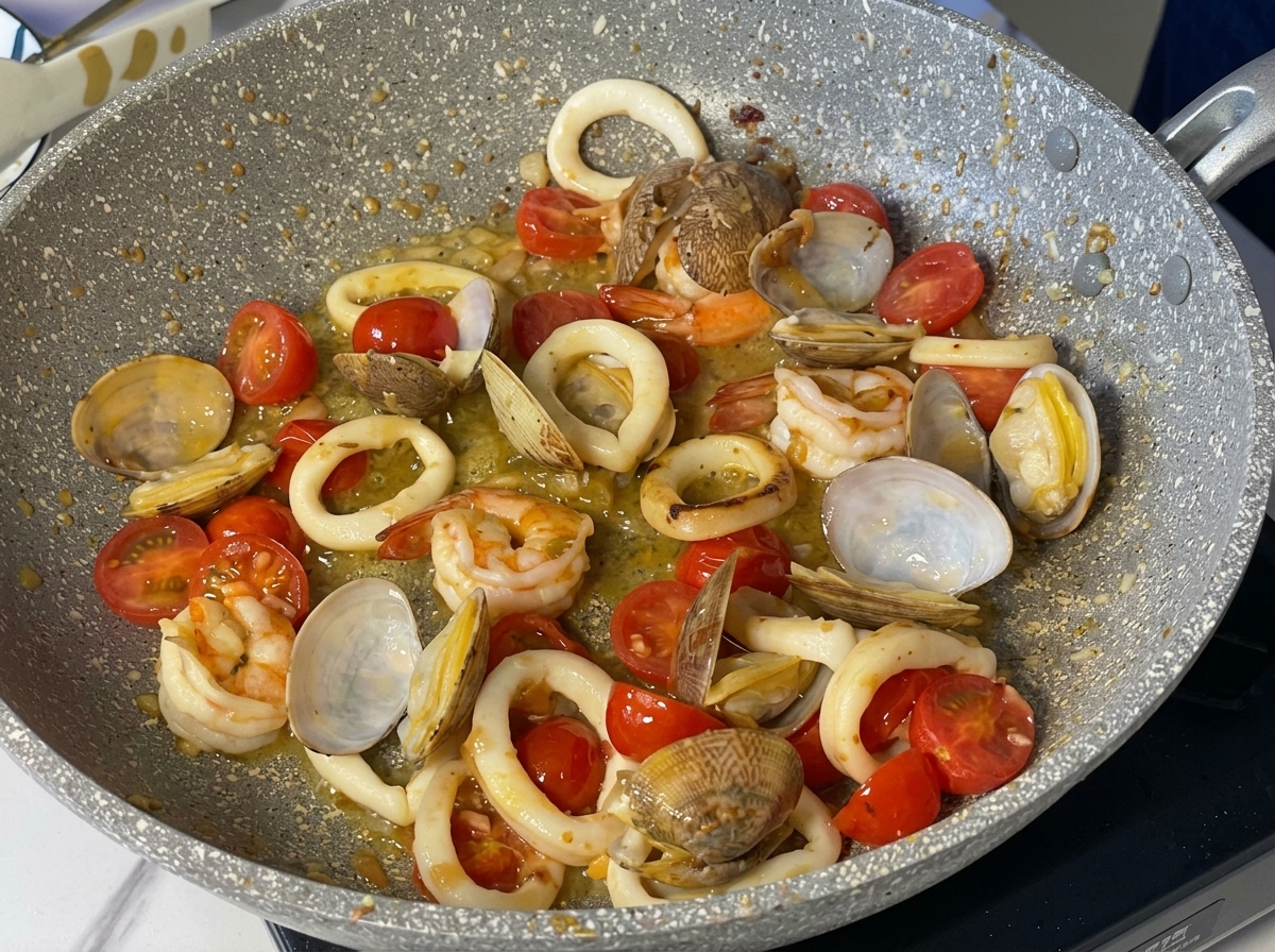 Gambas, calamares, almejas y tomates cherry hirviendo a fuego lento en una salsa de vino blanco y mantequilla.