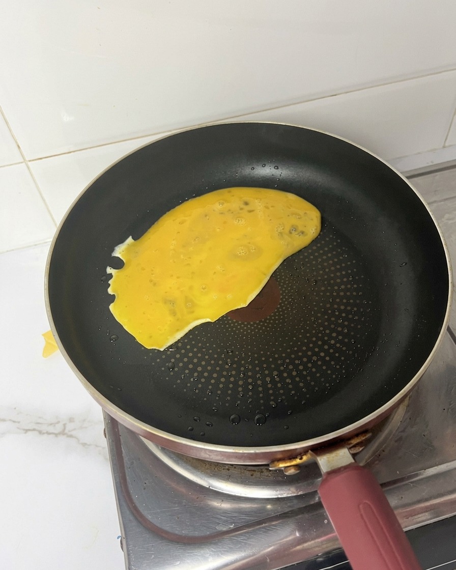 Mezcla de huevo batido vertiéndose y extendiéndose por una sartén caliente.