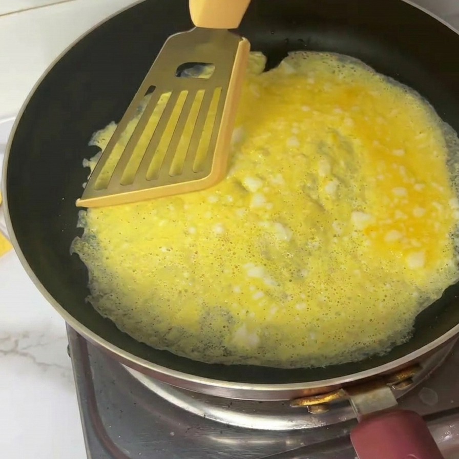 Una tortilla fina de huevo cortada en cuatro trozos con una espátula de metal en la sartén.