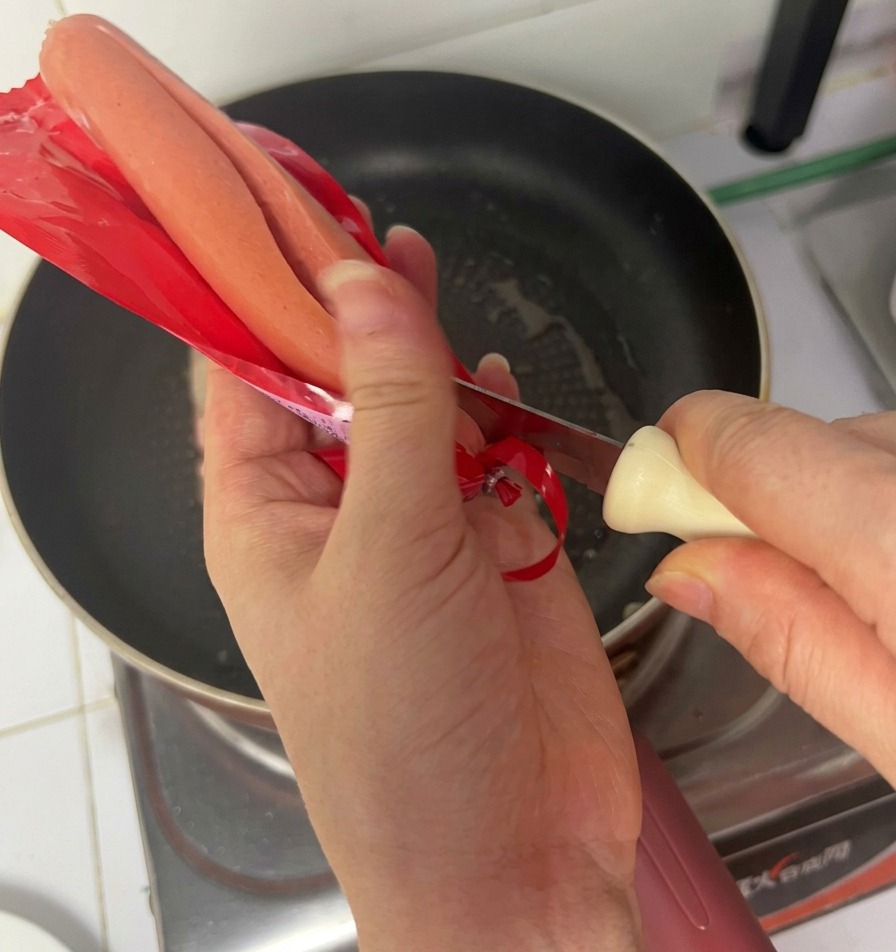 Manos abriendo un paquete de salchicha de jamón sobre la sartén con bacon.