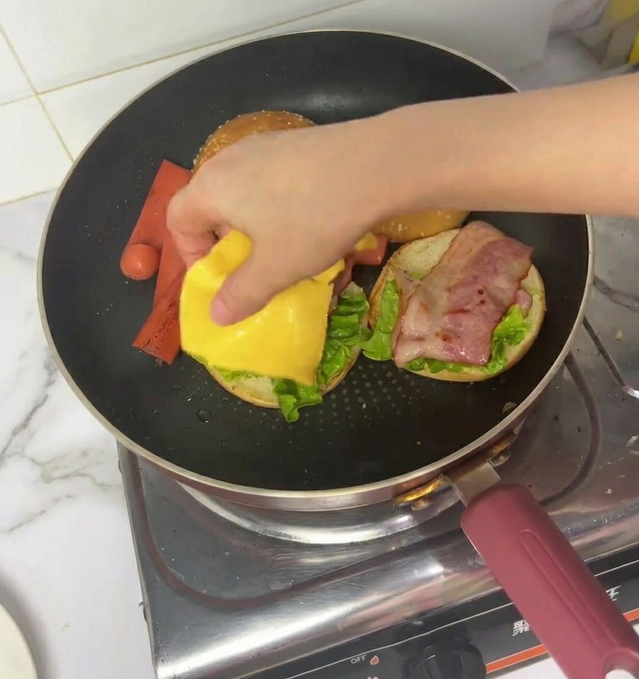 Una mano colocando una loncha de queso amarillo sobre la lechuga y el bacon.