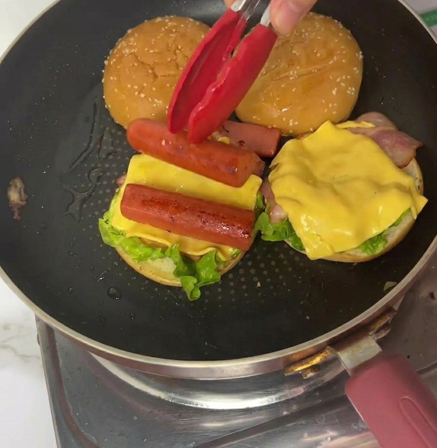 Un cuarto de tortilla de huevo colocándose sobre la hamburguesa con pinzas rojas.