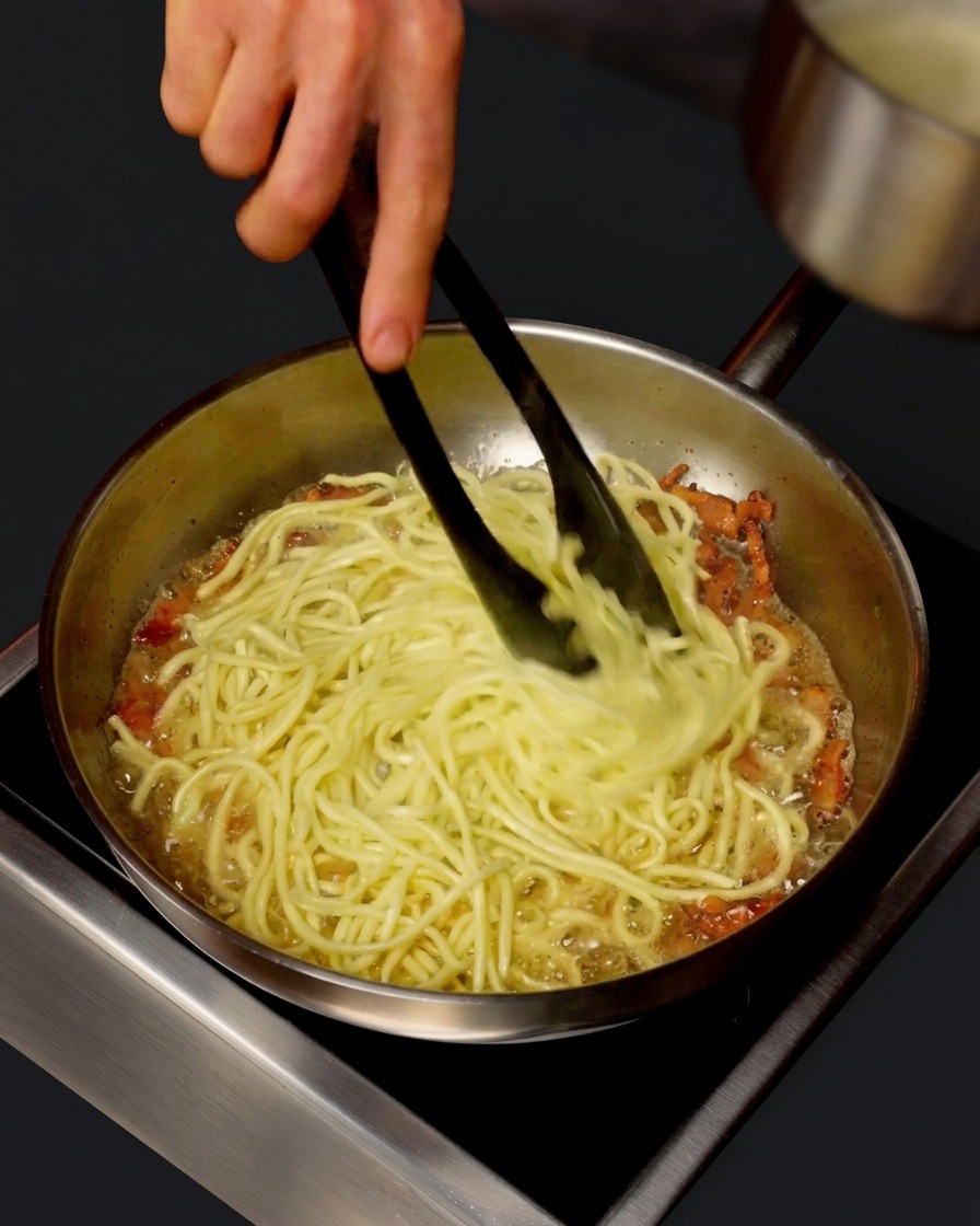 Un cazo vertiendo agua caliente de la pasta en una sartén con espaguetis.