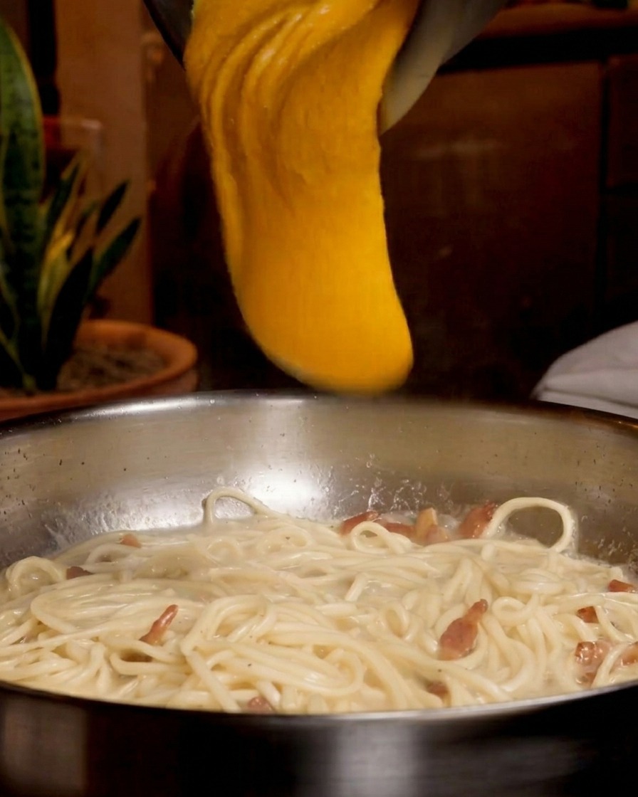 Una mezcla espesa de huevo y queso cayendo sobre una sartén con espaguetis.