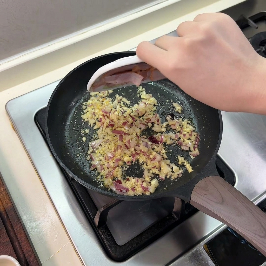 Bacon en tiras deslizándose desde un plato hacia la sartén con cebolla y ajo.