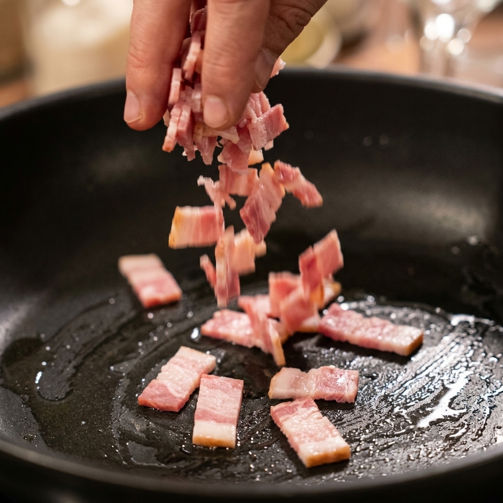 Mano echando pequeños trozos de bacon crudo en una sartén negra caliente y ligeramente engrasada.