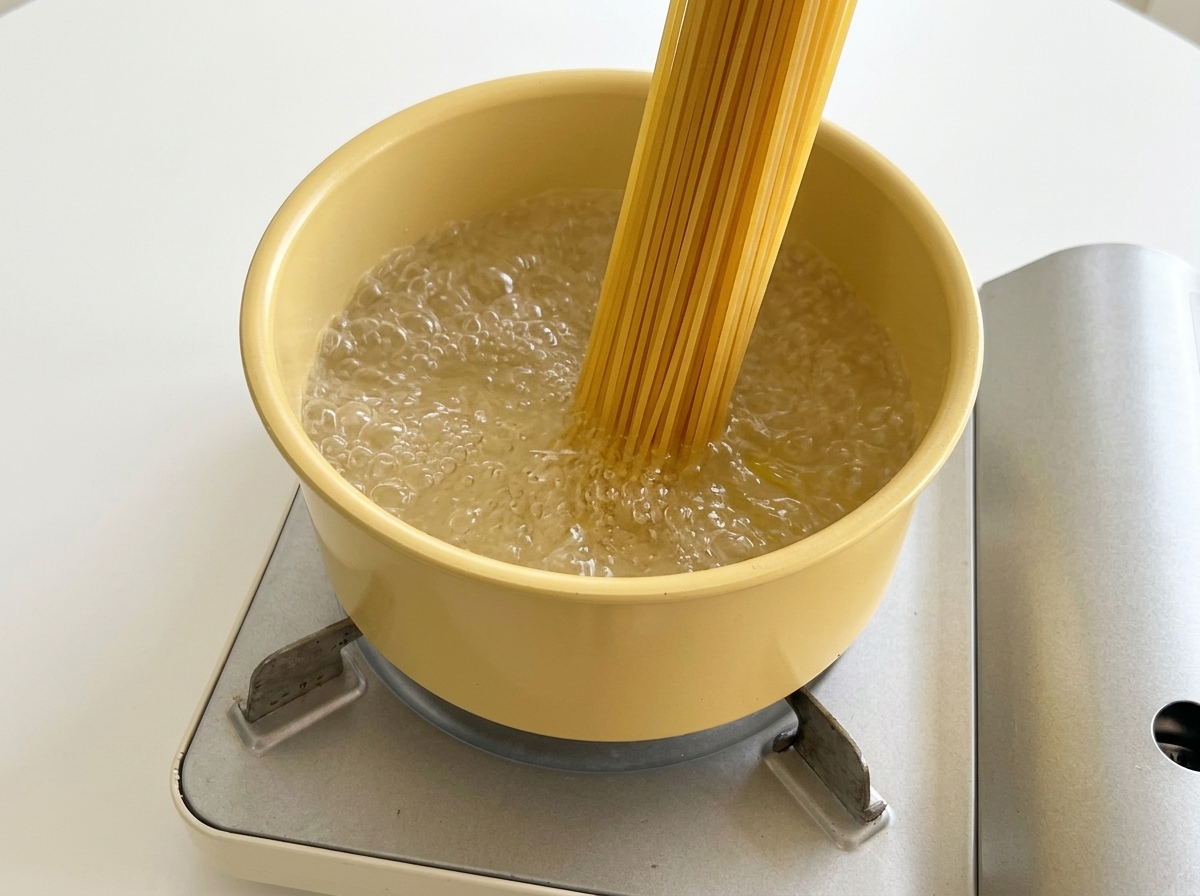 Colocando espaguetis secos en una olla amarilla llena de agua hirviendo.