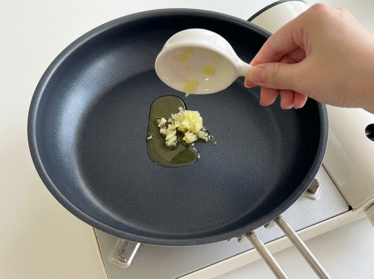 Vertiendo ajo picado desde un plato pequeño a una sartén negra caliente con aceite.