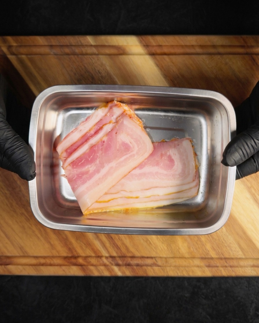 Tiras de bacón crudo colocadas en una bandeja metálica rectangular.